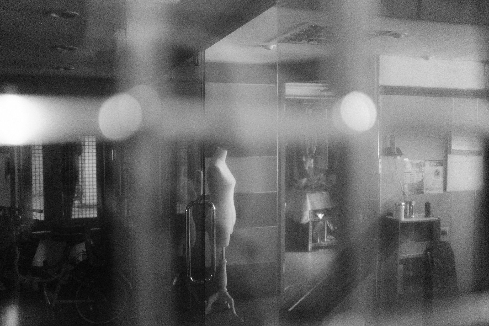 Dreamy black and white street photography with soft foreground bokeh, looking through a window at a mannequin inside a Taiwan shop