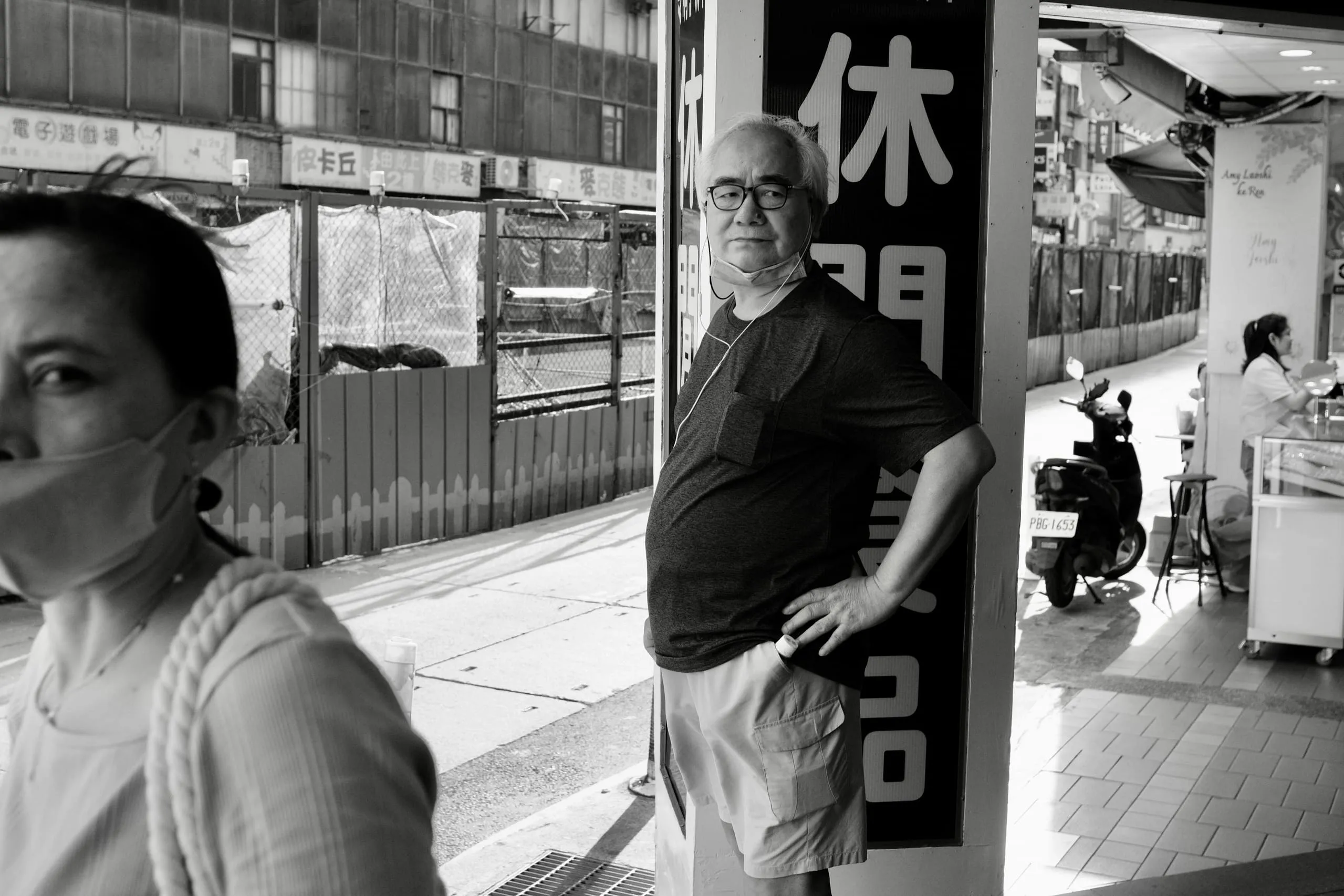 騎樓休閒招牌旁男子靠牆站著，前景女子半張臉經過，365 Project September 14