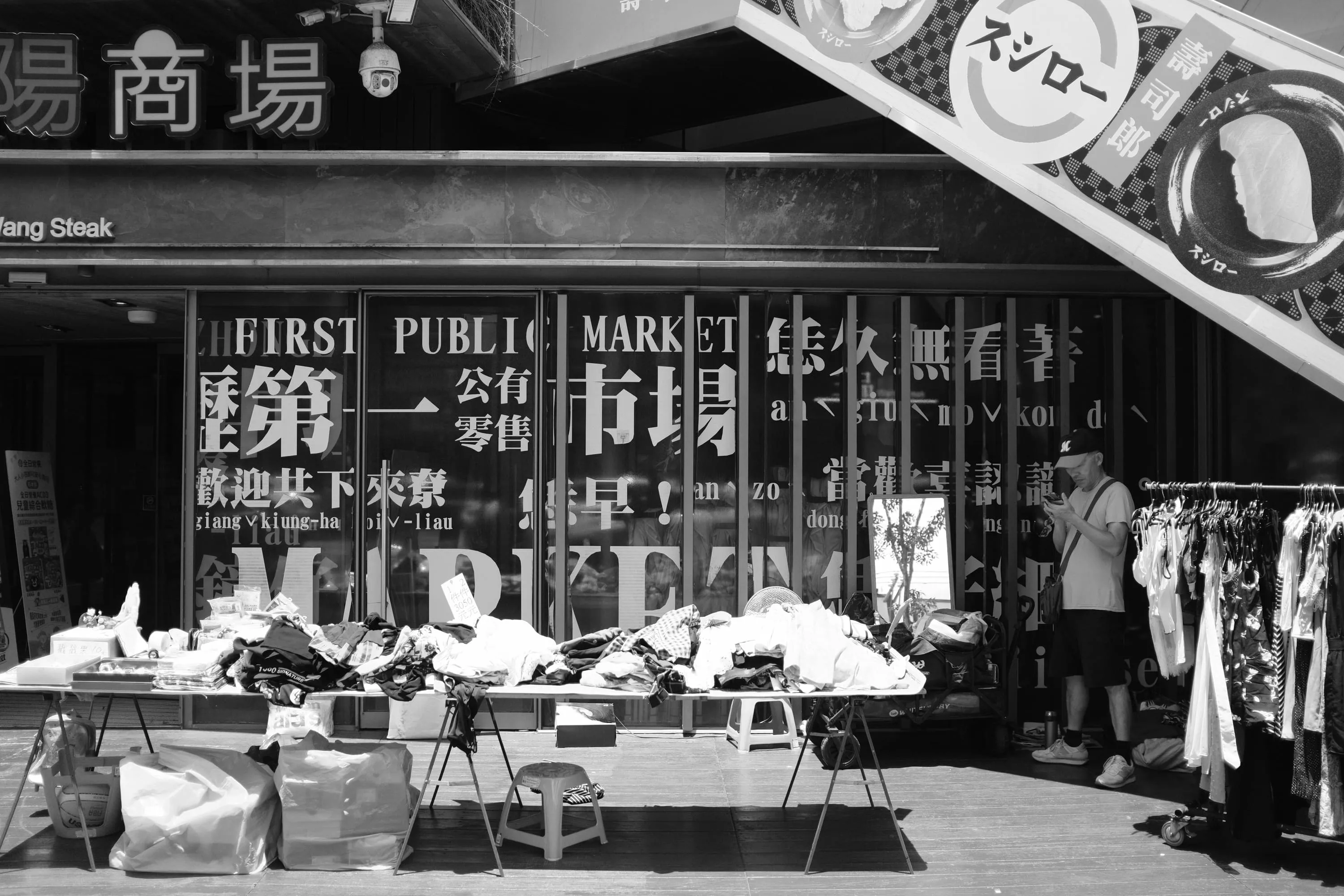 公共市場玻璃字樣前衣物攤位旁男子低頭看手機，365 Project September 10