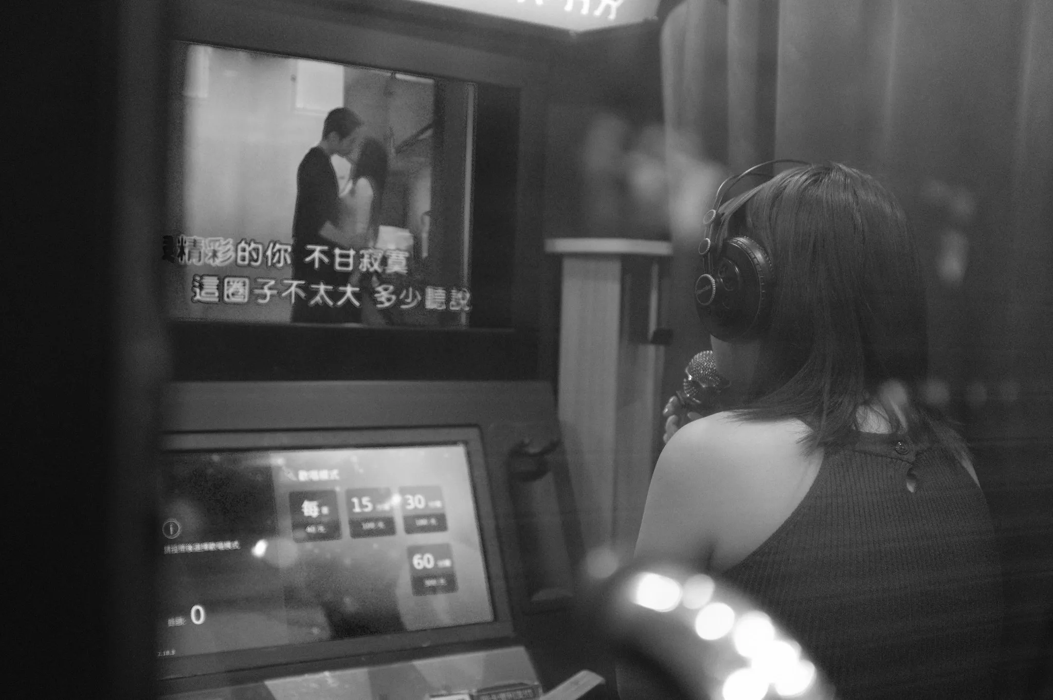KTV 包廂內女子戴著耳機手持麥克風面向螢幕，畫面字幕與點歌機同時亮起，365 Project October 2