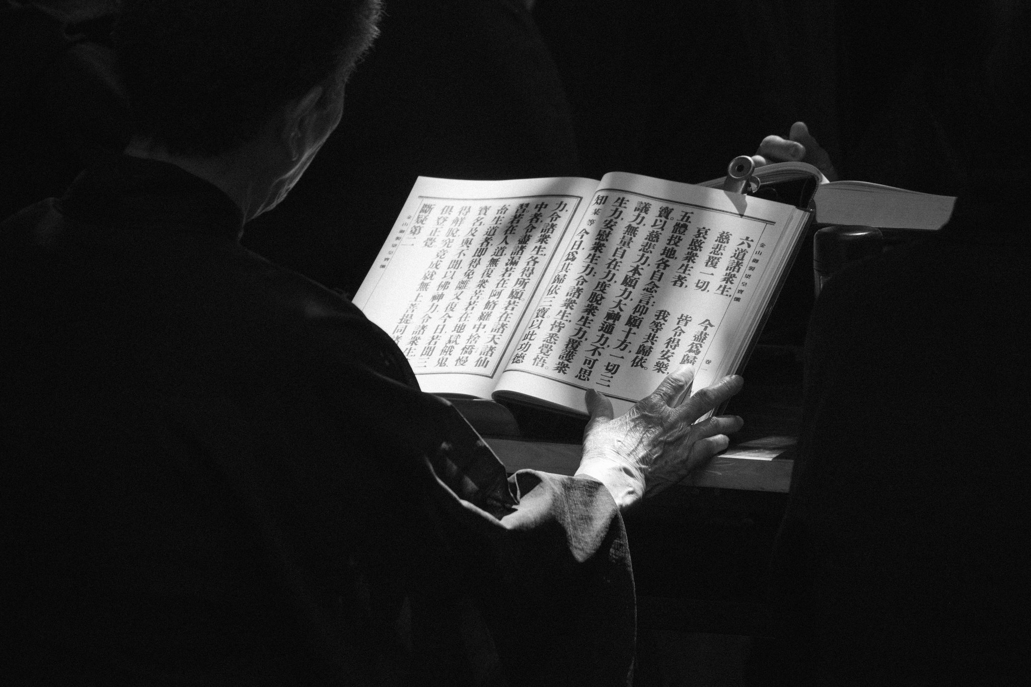 An elderly worshipper reading scripture under a focused pool of light