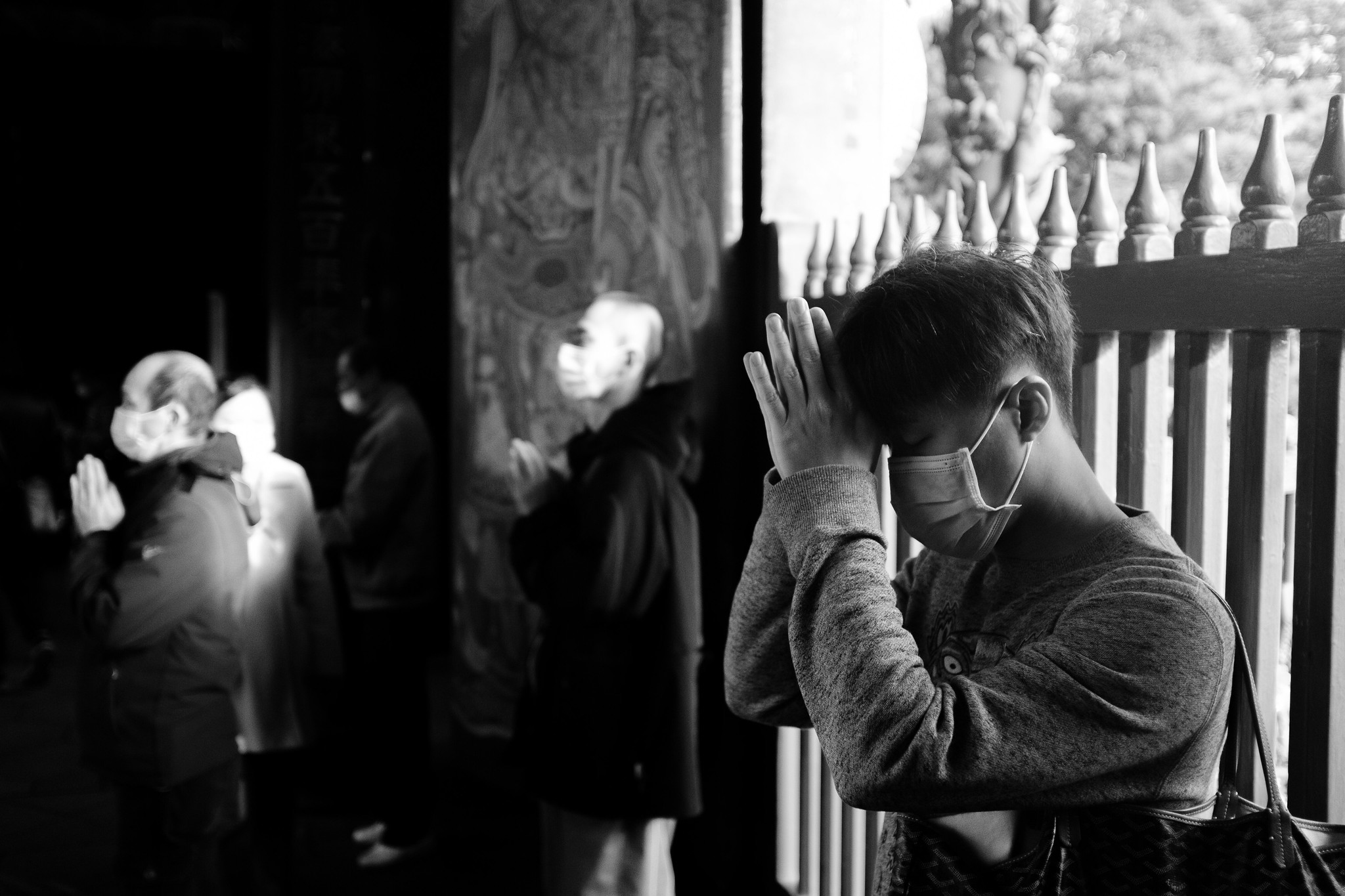 Masked child pressing hands together in prayer inside a Taiwan temple