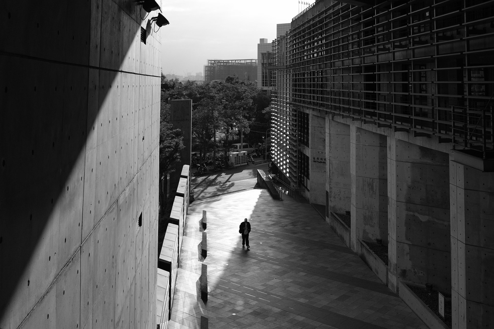 Black and white architectural scene in Taiwan with strong shadow geometry, concrete walls, and a lone figure crossing a bright courtyard