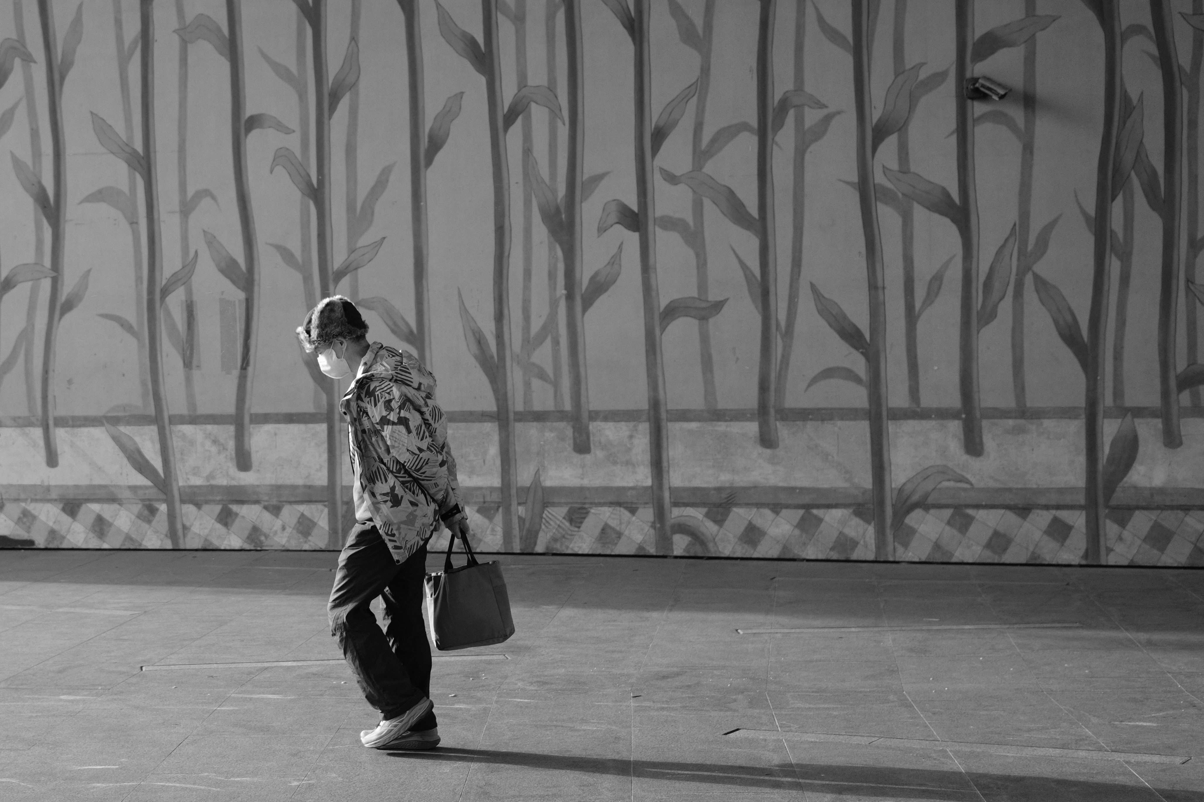 Black and white urban composition of a pedestrian walking past a bamboo-patterned wall in Taiwan