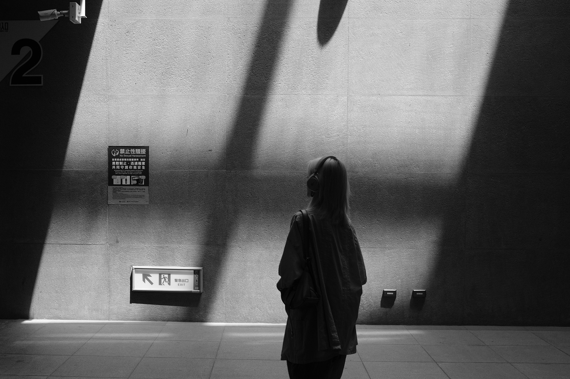 Black and white street photo of a lone figure standing beneath strong architectural shadows in Taiwan