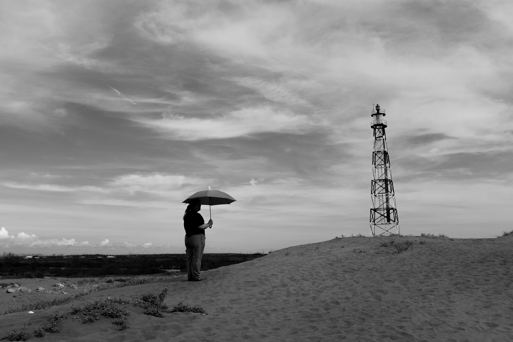 Black and white coastal scene with an adult and child standing in shallow intertidal water beneath an open sky