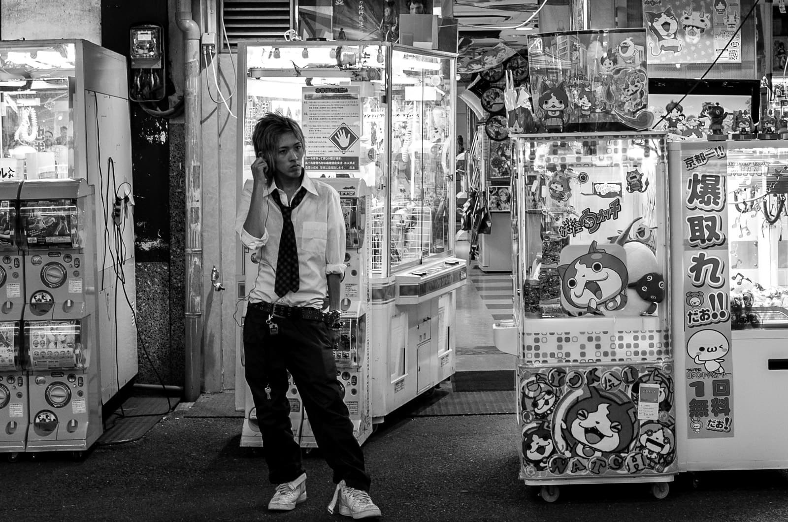 Black and white arcade entrance in Japan with an attendant on the phone between capsule toy and claw machines