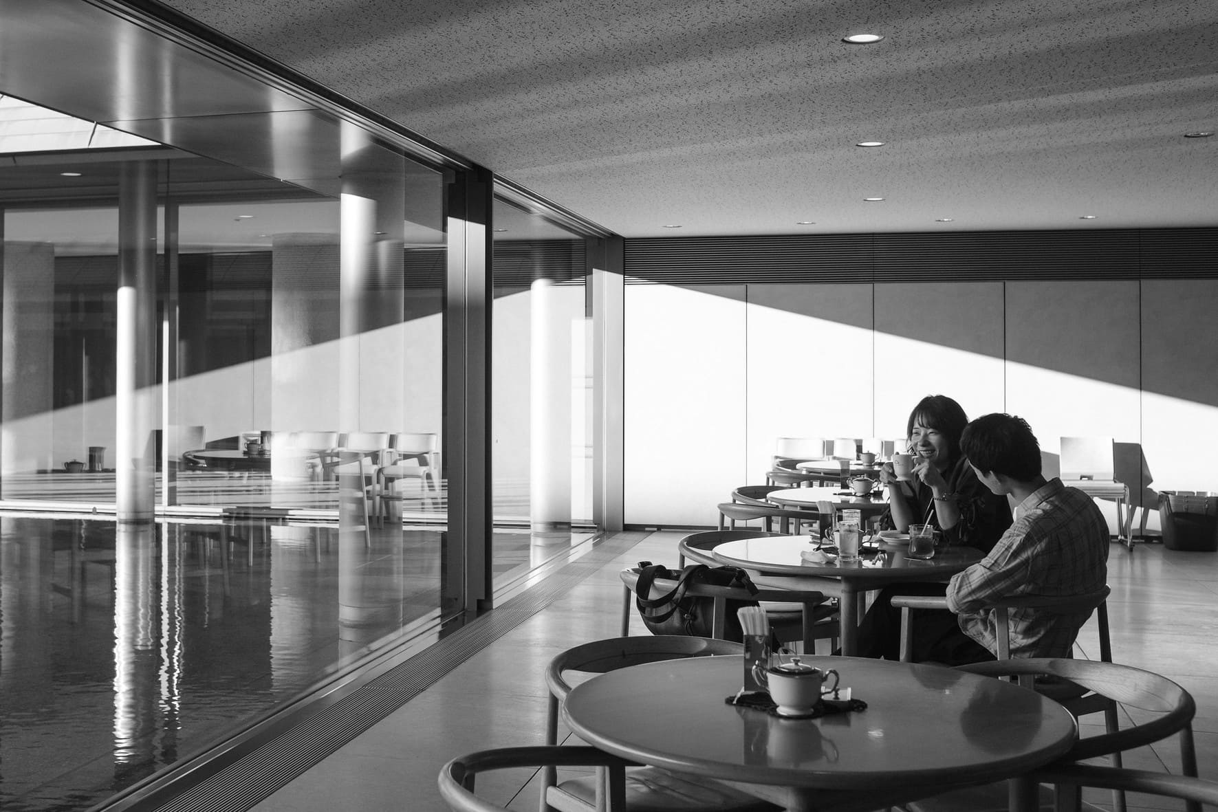 Black and white cafe interior in Japan with two people talking beside bright window reflections