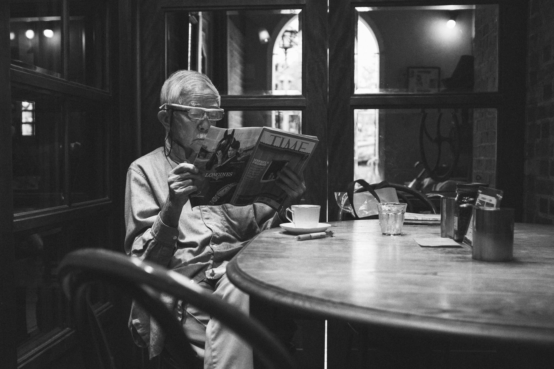 Black and white cafe scene in Japan with an older man reading a magazine at a wooden table