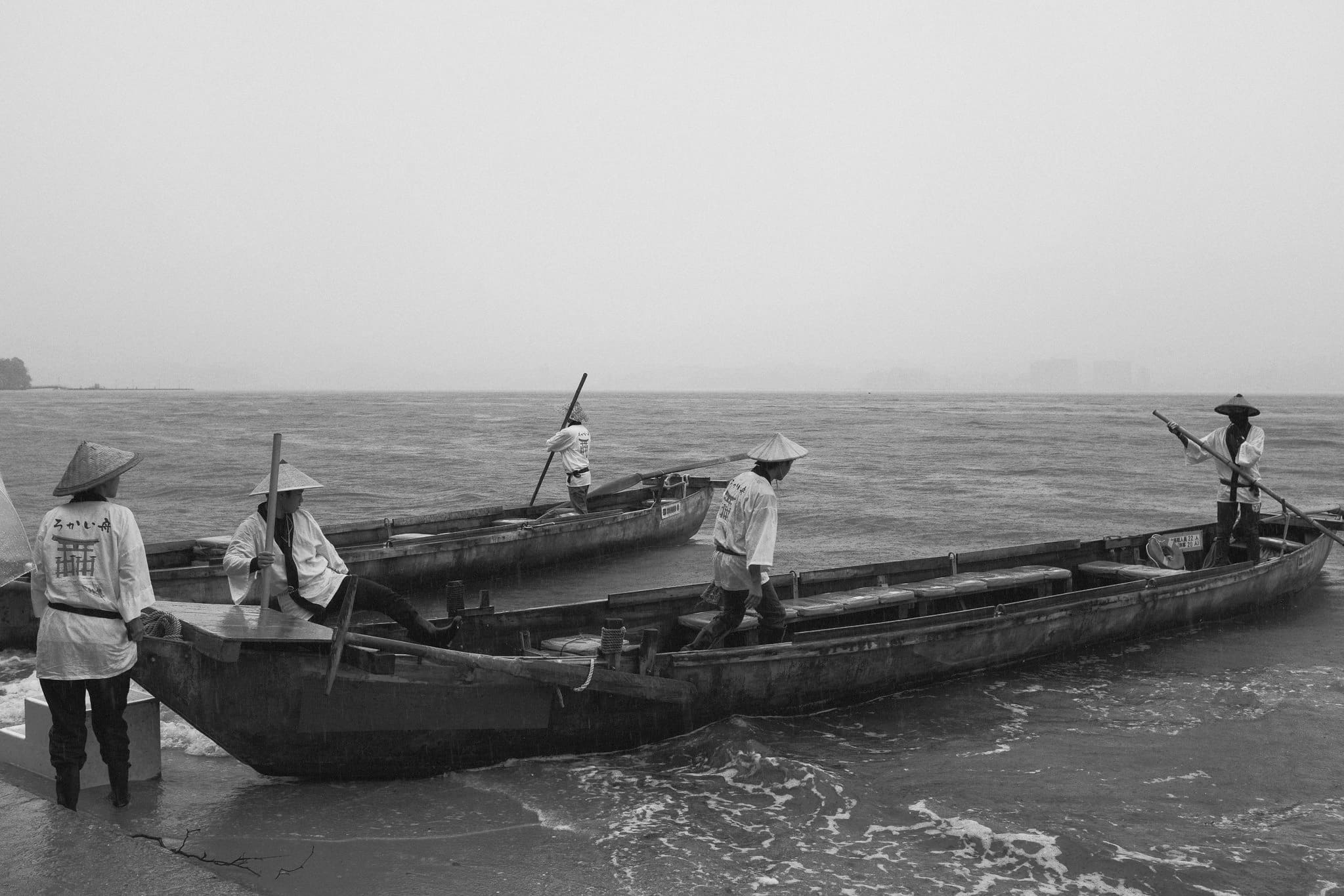Black and white coastal scene in Japan with boatmen maneuvering wooden boats in shallow water