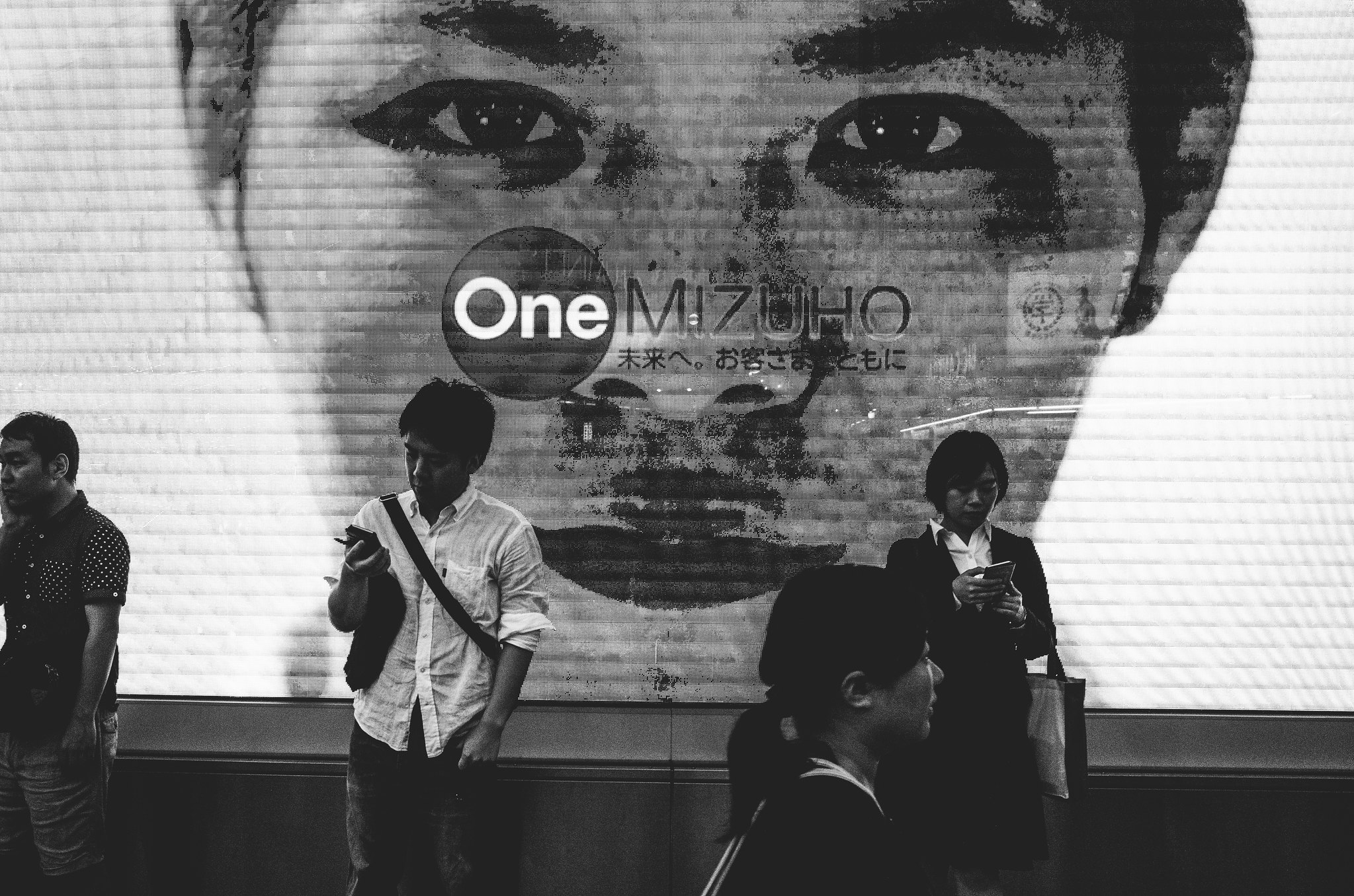 Black and white commuters standing before a large digital billboard in Japan