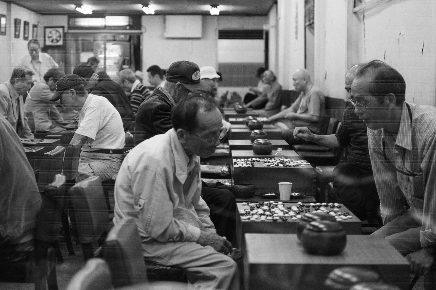 Black and white view through a window in Japan of several men playing Go at closely spaced tables