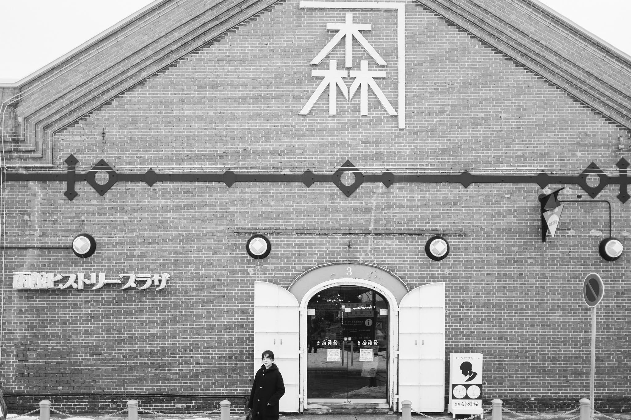 Black and white view of a pedestrian outside the Hakodate History Plaza brick warehouse in Japan