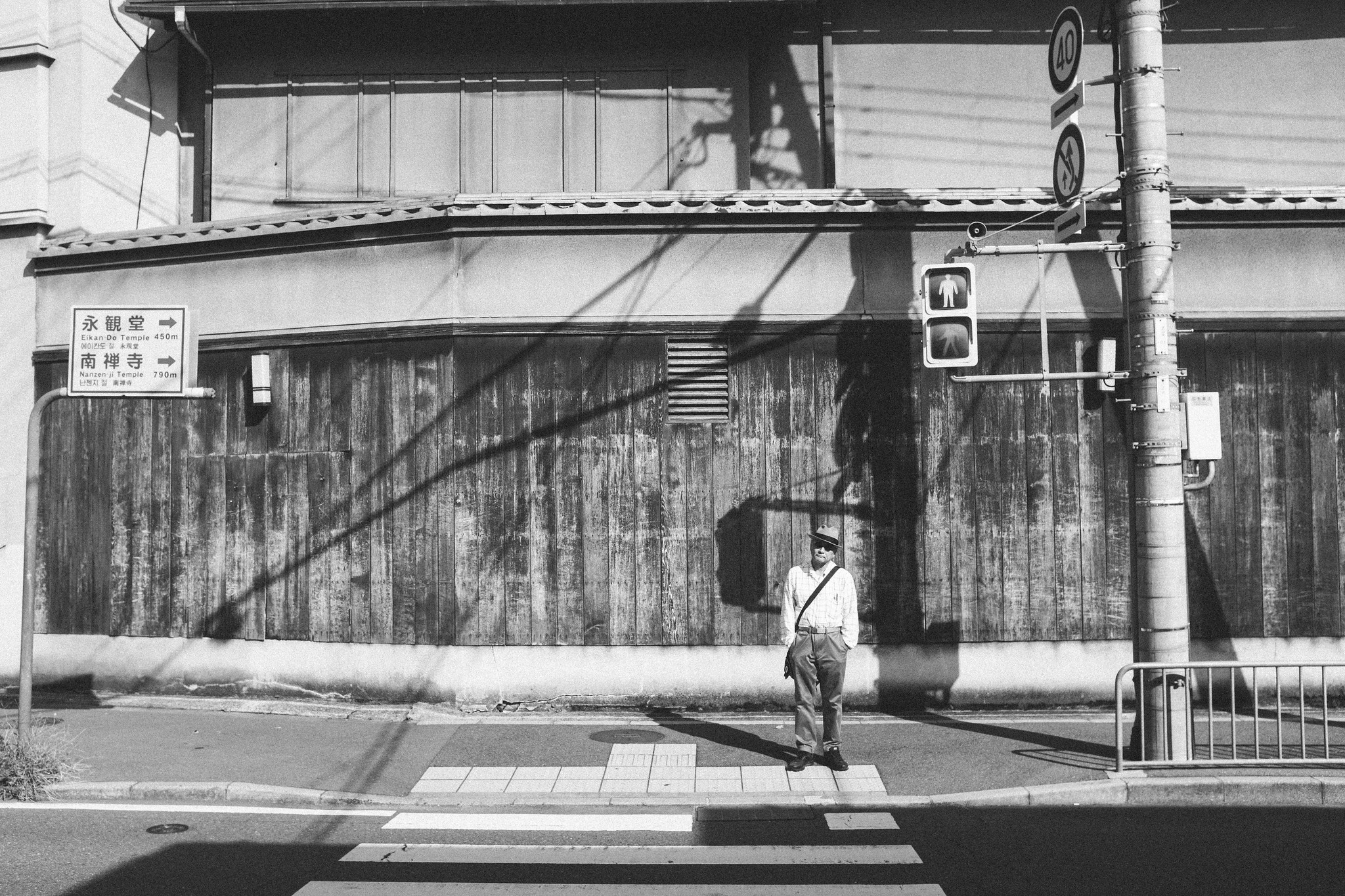 Black and white Japanese street scene with a lone pedestrian crossing in front of a wooden facade