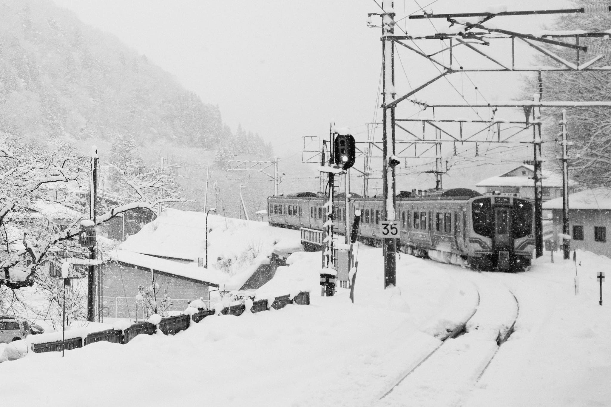Black and white train rounding a snow-covered railway curve in the Japanese mountains