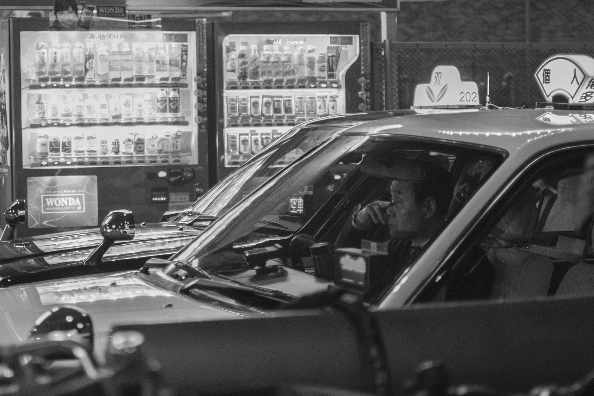Black and white night scene in Japan with a taxi passing illuminated vending machines