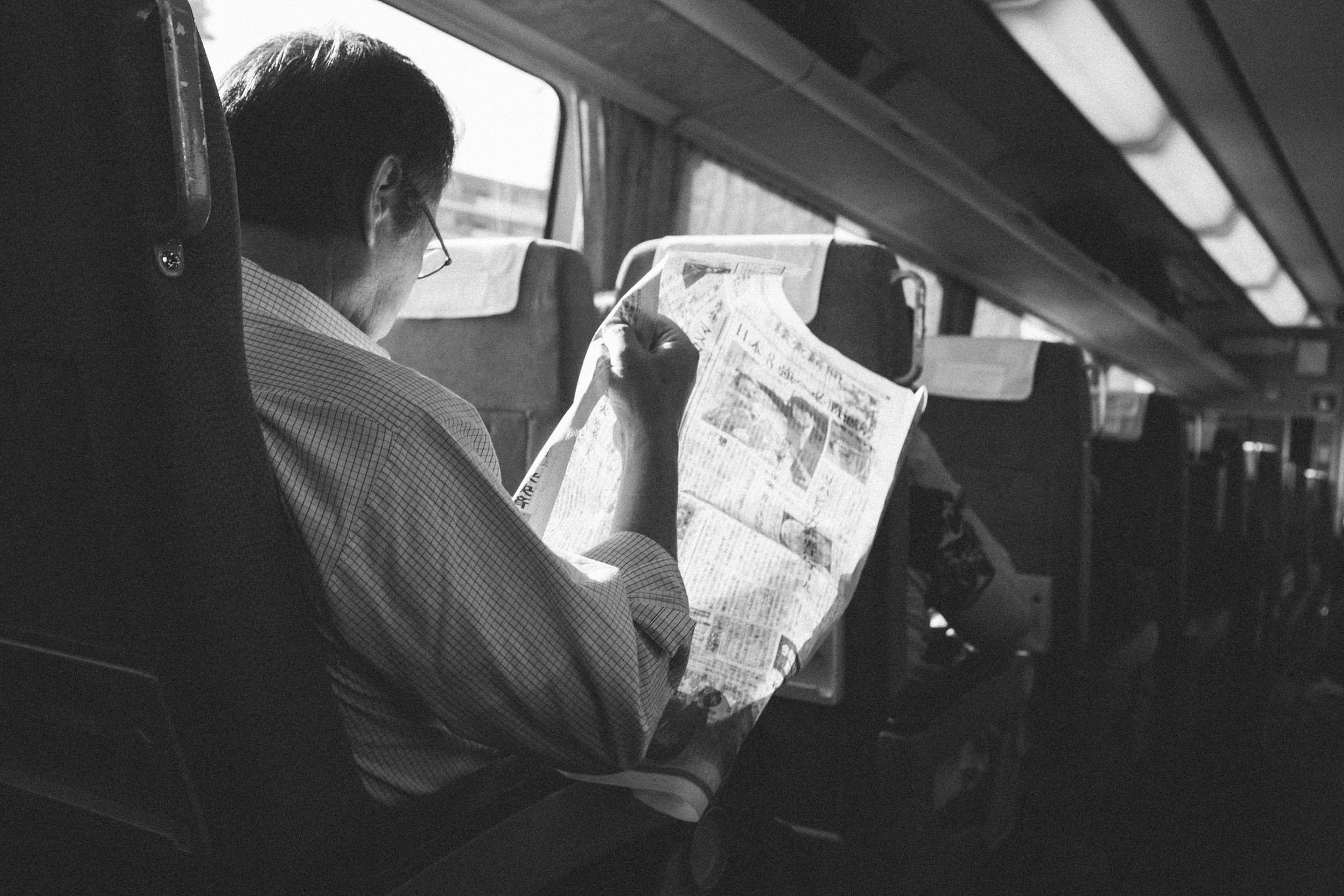 Black and white train interior in Japan with a passenger reading a folded map by the window
