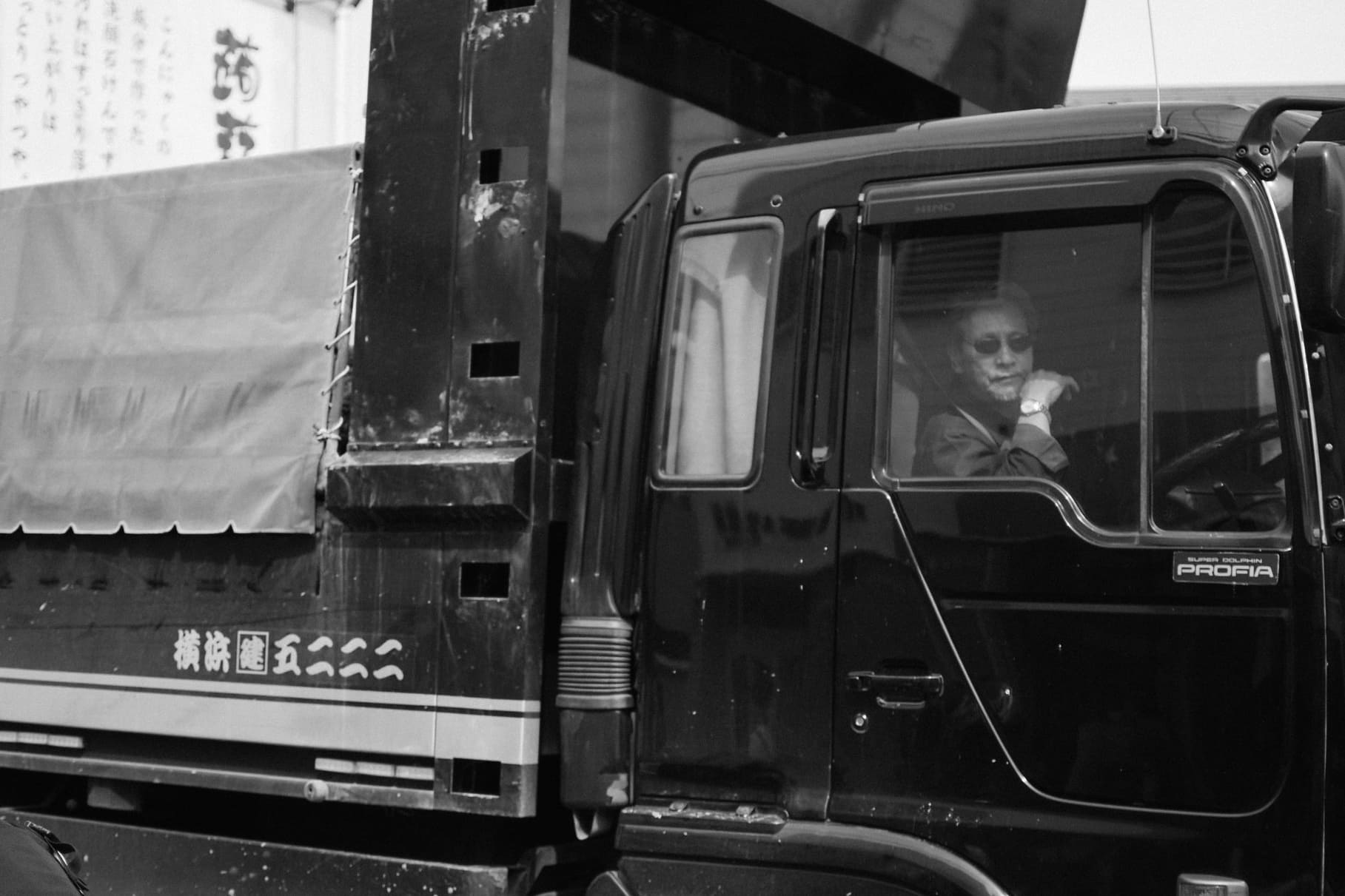 Black and white street portrait in Japan of a truck driver resting an arm beside the cab window