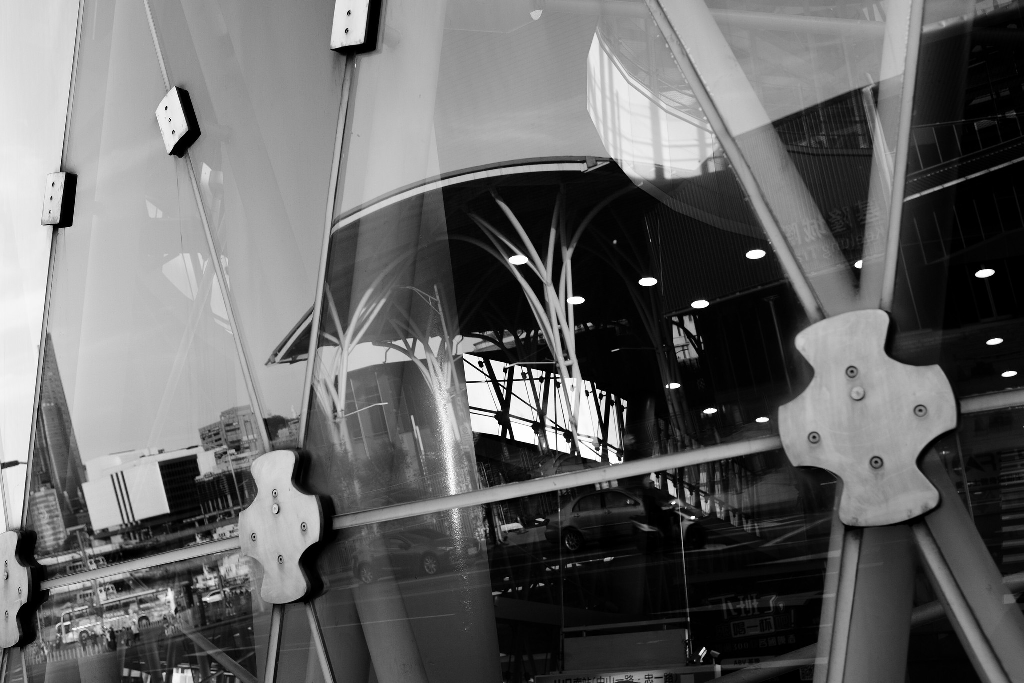 Black and white street photograph of glass architecture reflecting traffic and city structures in Keelung, Taiwan