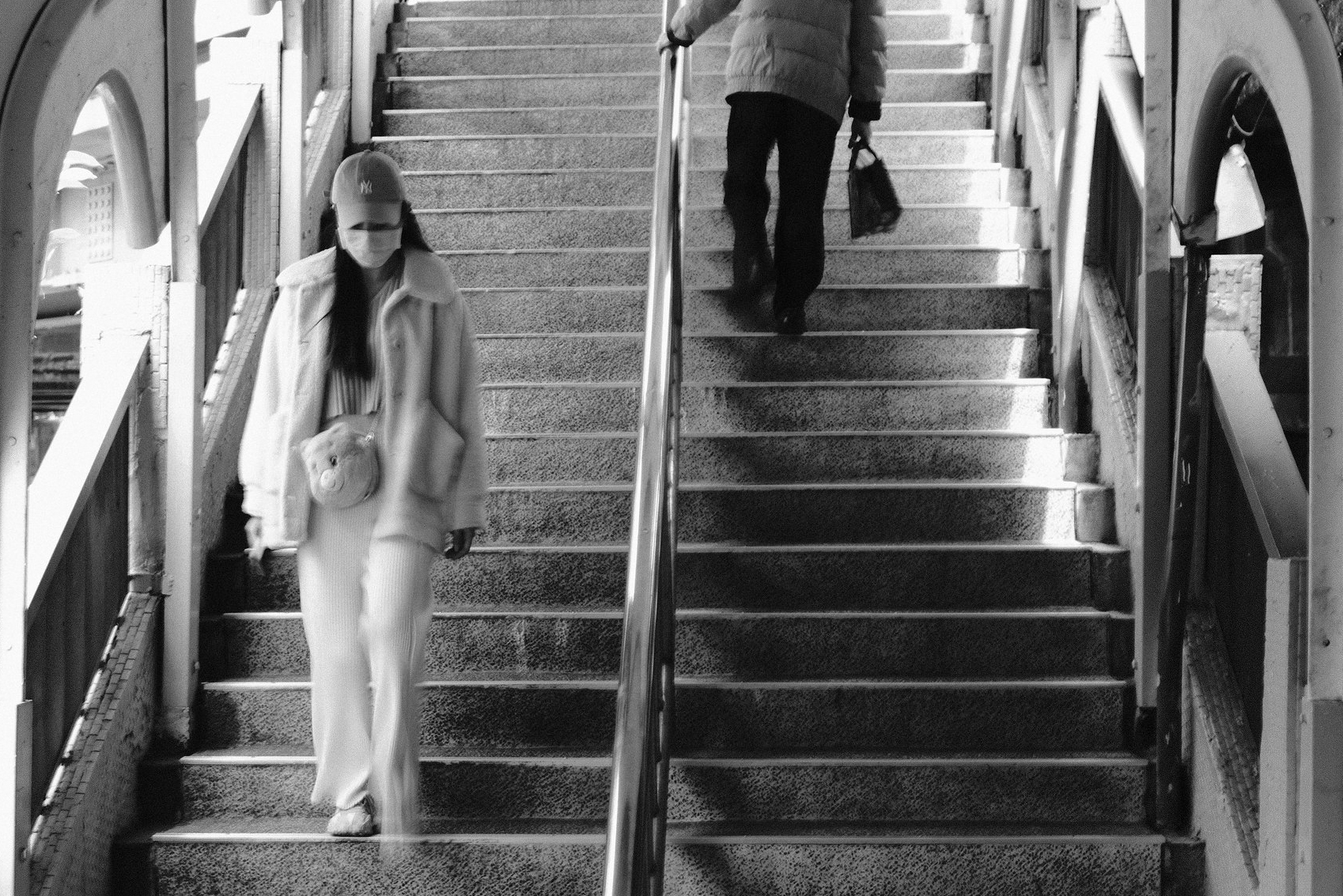 Black and white street photograph of two pedestrians moving in opposite directions on a sunlit footbridge staircase in Keelung, Taiwan