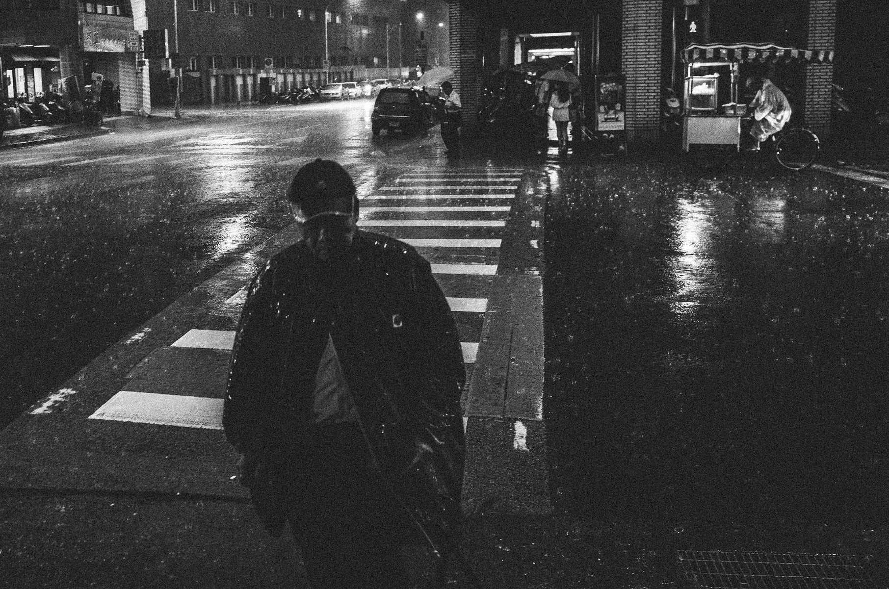 Black and white rainy crosswalk scene with a lone pedestrian carrying an umbrella in Taiwan
