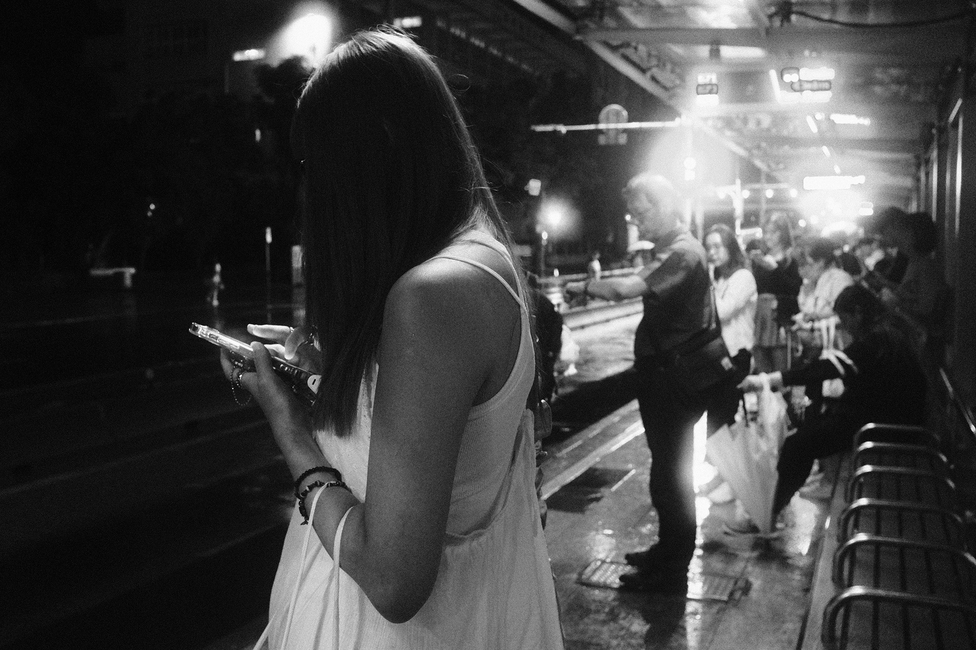 Atmospheric black and white rainy night street photo of people waiting near a bus stop in Taiwan