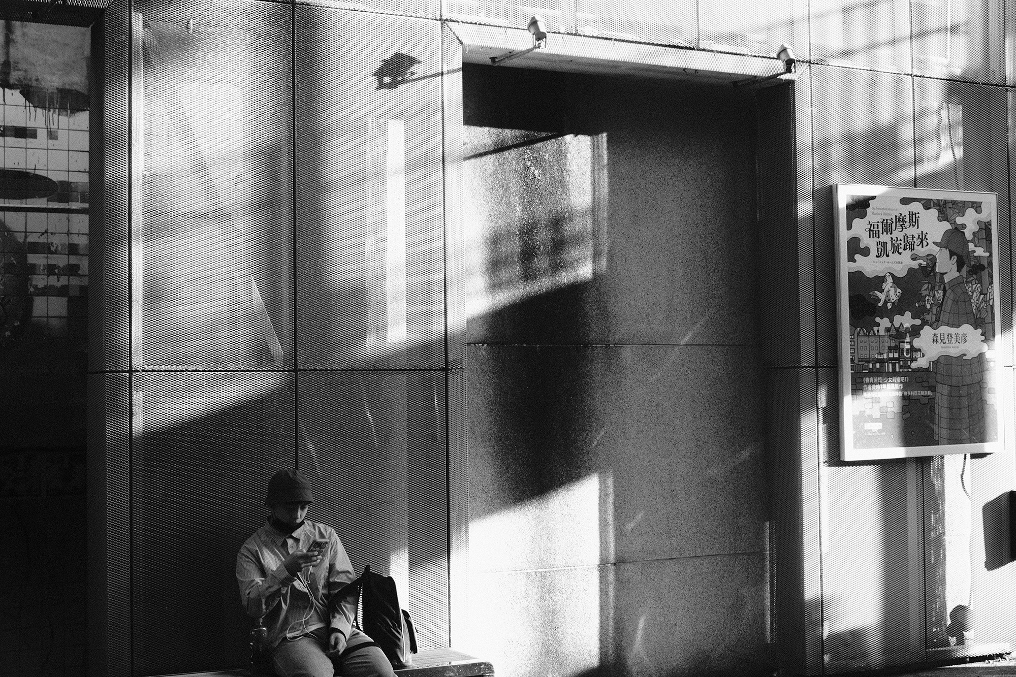 Black and white architectural street photo capturing sharp shadows on a mesh facade with a person sitting on a bench in Taiwan