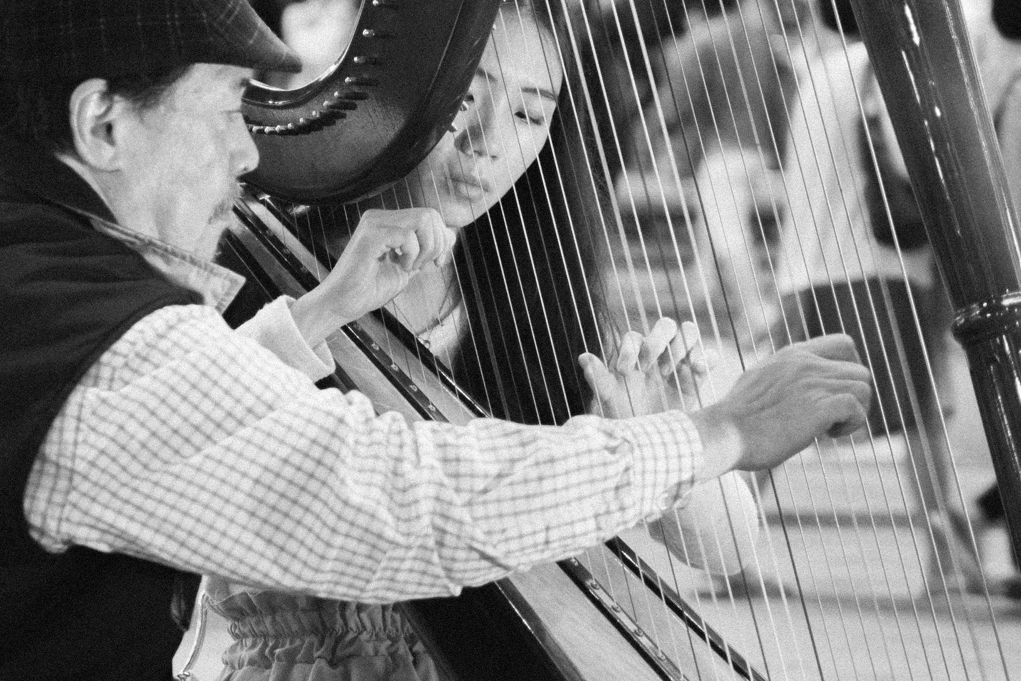 Black and white photograph of a harpist playing beneath the strings of a concert harp