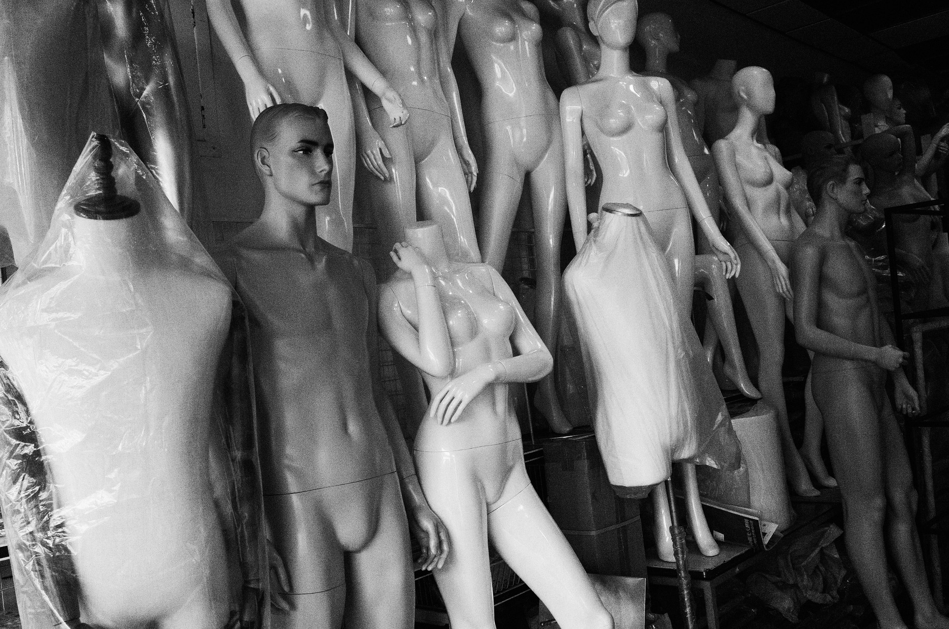Black and white street photograph of a mannequin display crowded with figures in a dark shop window