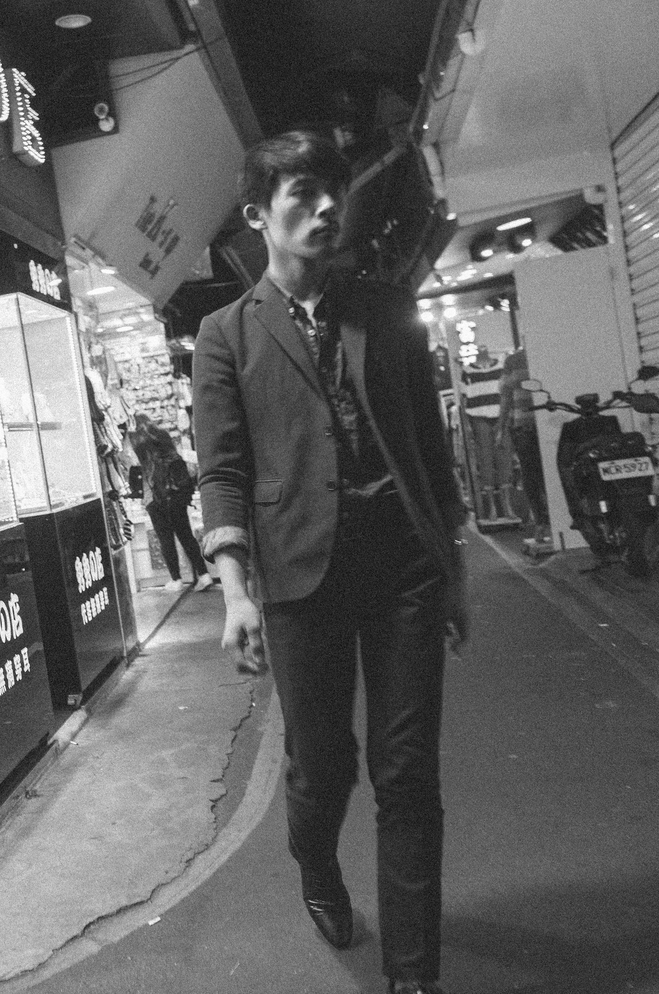 Black and white vertical street photograph of a man in a suit walking through a brightly lit shopping arcade