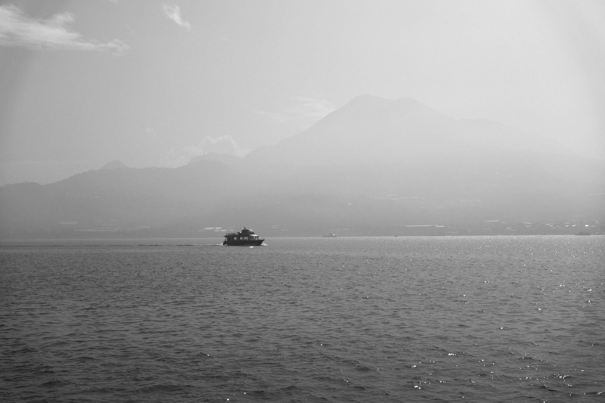 Black and white photograph of a small ferry crossing the Tamsui River with misty mountains in the background