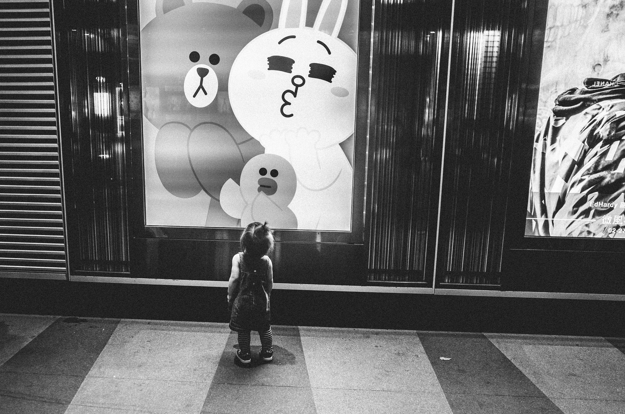 Black and white Xinyi street scene with a passerby beneath a bright character display window in Taipei